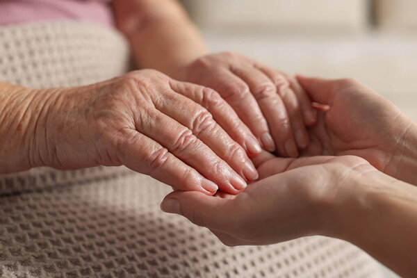 Caregiver supporting senior woman on light background, closeup. Elderly care