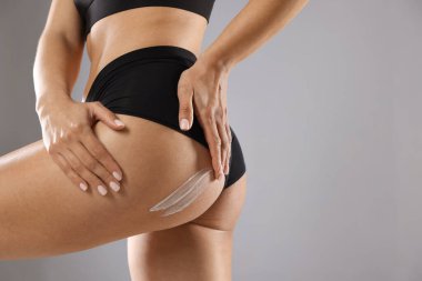 Gri arka plana anti-selülit kremi süren bir kadın. Yakın plan. Metin için boşluk