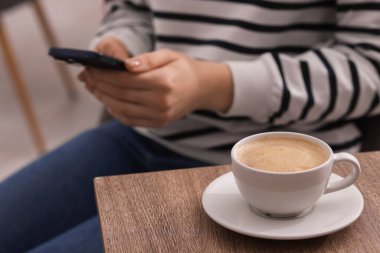 Kahve molası sırasında akıllı telefon kullanan bir kadın, kapalı masa, yakın plan.