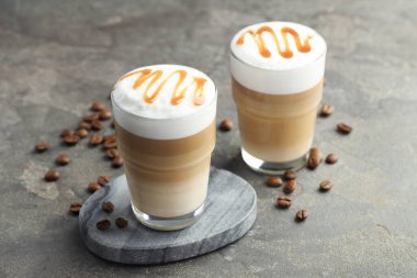 Bardakta latte macchiato ve gri masada kahve çekirdekleri, yakın plan.