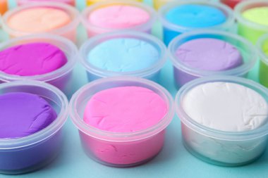 Açık mavi arka planda plastik kavanozlardaki farklı renkli modelleme killeri, yakın plan