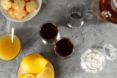 Gri desenli masada, düz yerde servis edilen metal tutacaklı çay bardakları.