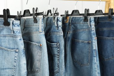 Many stylish jeans hanging from rack on white background, closeup