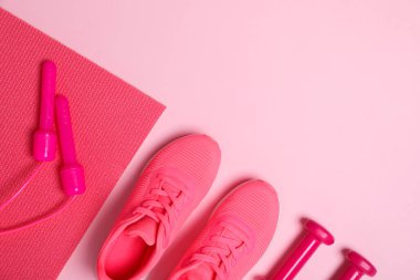 Spor malzemeleri. İp atlama, paspas, spor ayakkabıları ve pembe arka plandaki dambıllar, düz uzanma. Metin için boşluk