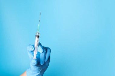 Doktor açık mavi arka planda şırınga tutuyor, yakın plan. Metin için boşluk