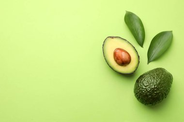 Taze olgun avokadolar ve açık yeşil arka planda yapraklar, düz. Metin için boşluk