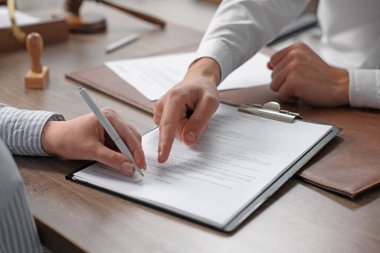 Belgeye işaret eden noter ve müşteri, kapalı oturulan ahşap masaya imza atıyor, yakın plan