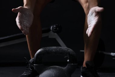 Siyah arka planda kettlebell eğitimi almadan önce talk pudrasıyla el çırpan adam, yakın plan.