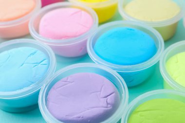 Açık mavi arka planda plastik kavanozlardaki farklı renkli modelleme killeri, yakın plan