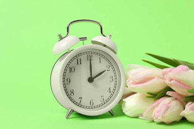 Bahar geldi. Çalar saat ve yeşil arka planda güzel laleler.