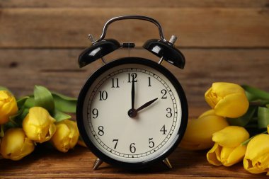 Bahar geldi. Çalar saat ve ahşap masada güzel laleler.