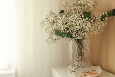 Beyaz duvarın yanındaki çekmecelerin üstündeki vazoda güzel çigila çiçekleri ve okaliptüs dalları. Metin için boşluk