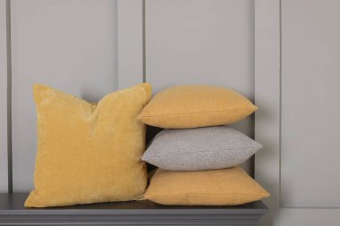 Gri duvarın yanındaki çekmecelerin üzerindeki yumuşak dekoratif yastıklar.