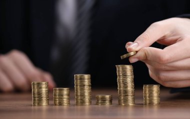 Adam ahşap masadaki para yığınlarına para koyuyor, yakın plan.