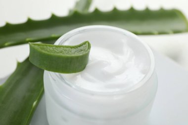 Aloe vera özütüyle nemlendirici krem ve beyaz arkaplanda yapraklar, yakın plan.