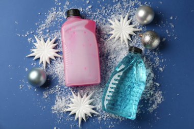 Plastik şişelerde antifriz, takılar, dekoratif kar taneleri ve mavi arka planda buz, düz bir zemin.