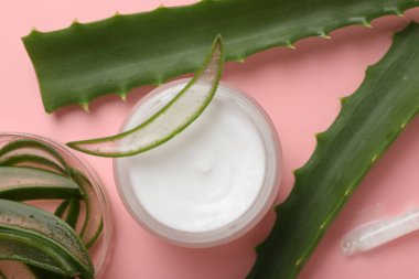 Kavanozda aloe vera özütüyle nemlendirici krem ve pembe arka planda yapraklar.