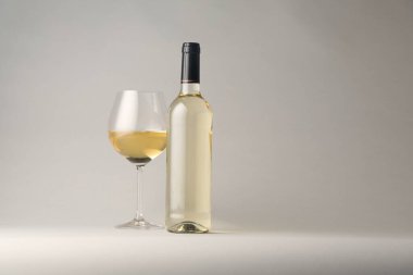 Bardakta lezzetli beyaz şarap ve açık gri arka planda şişe, metin için yer