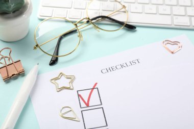 Açık mavi arkaplanda işaretli işaretli kontrol kutusu, klavye, gözlük ve kağıt ataçları, yakın plan