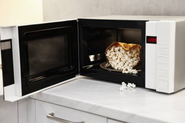 Mikrodalga fırını aç, mutfakta beyaz mermer tezgahta patlamış mısır torbası var.