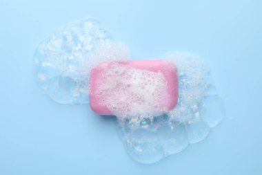 Açık mavi arkaplanda köpük olan sabun çubuğu, üst görünüm