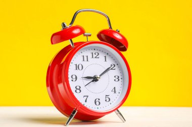 Sarı arka planda beyaz ahşap masada kırmızı bir çalar saat.