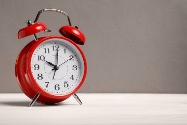 Gri arkaplana karşı beyaz ahşap masa üzerinde bir kırmızı alarm saati, metin için boşluk