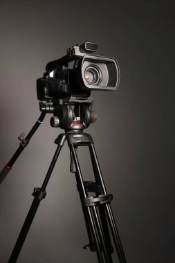Gri arka planda tripodu olan modern video kamera