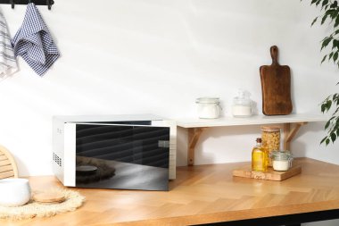 Mikrodalga fırını aç. Yiyecek ürünleri ve mutfak gereçleri içeride, ahşap masada.