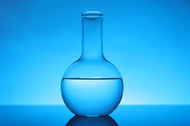 Ayna yüzeyinde sıvı bulunan matara açık mavi arka planda. Laboratuvar ekipmanları