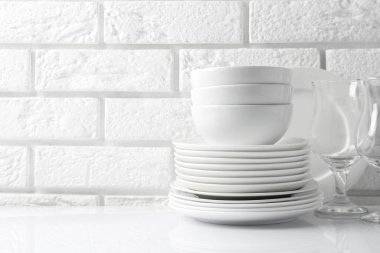 Tuğla duvarın yanındaki beyaz masada farklı temiz bulaşık takımları. Metin için boşluk