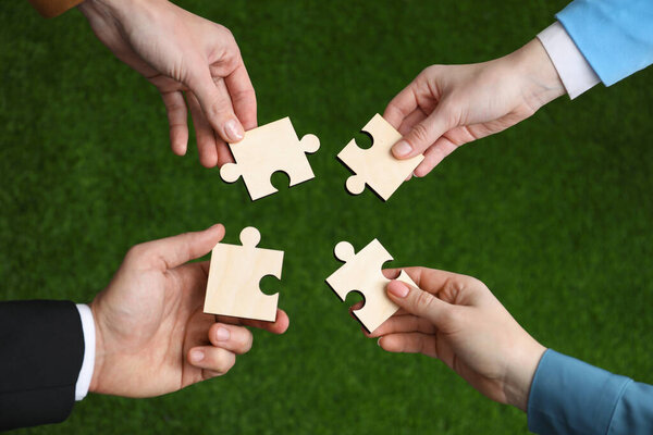 Teamwork. Group of people putting puzzle pieces together on blurred background, top view