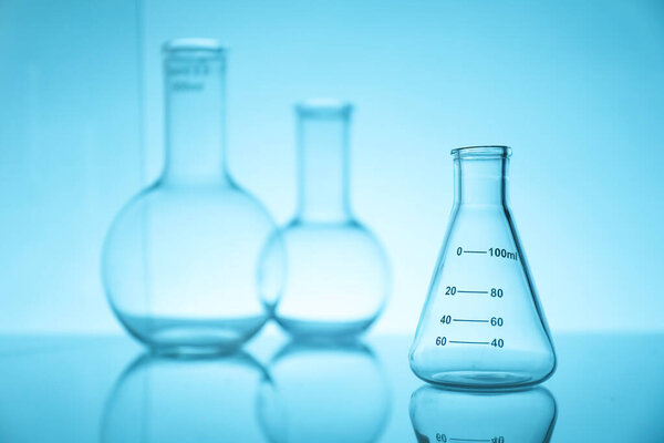 Empty flasks on mirror surface against light blue background. Laboratory equipment