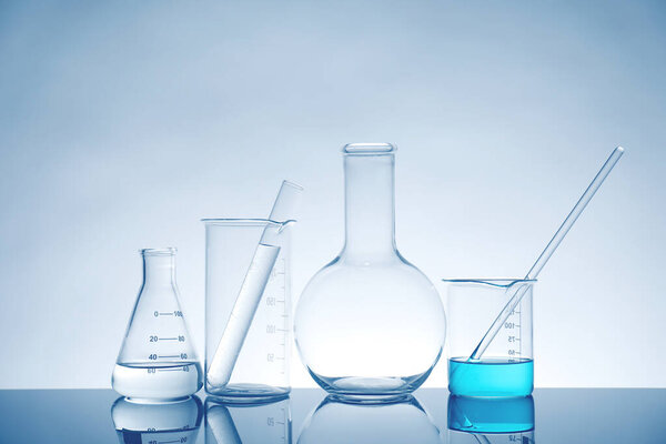 Laboratory glassware with liquid on mirror surface against light background