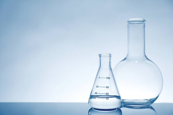 Laboratory glassware with liquid on mirror surface against light background, space for text