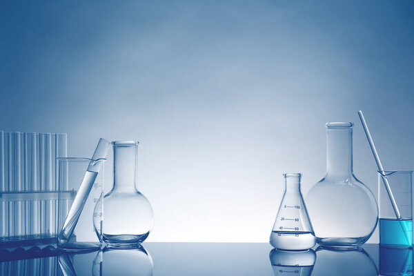Laboratory glassware with liquid on mirror surface against light background