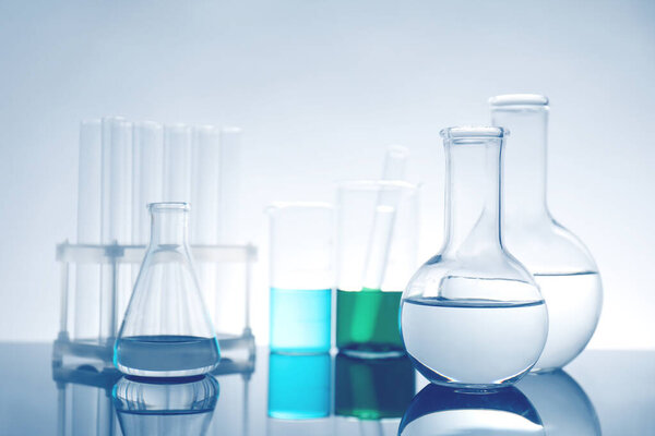 Laboratory glassware with liquid on mirror surface against light background
