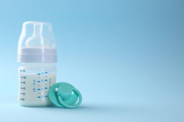 Açık mavi zemin üzerinde süt ve emzik ile beslenme şişesi, metin için boşluk