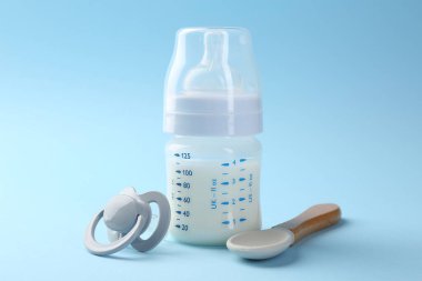 Açık mavi arka planda süt, kaşık ve emzik ile beslenme şişesi