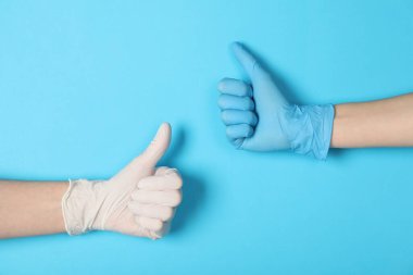 Tıbbi eldivenli doktorlar açık mavi arka planda baş parmak gösteriyor, yakın plan.