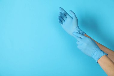 Doktor açık mavi arka plana tıbbi eldiven takıyor, yakın plan. Metin için boşluk