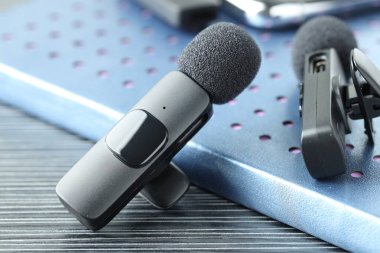 Lavalier mikrofonlar ve siyah ahşap masanın üzerindeki defter, yakın plan.