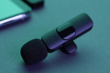 Lavalier mikrofon ve kablosuz alıcısı olan akıllı telefon karanlık masada neon ışıklarda, yakın plan.