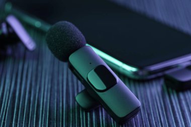 Lavalier mikrofon ve kablosuz alıcısı olan akıllı telefon. Karanlık ahşap masa, neon ışıklar, yakın plan.