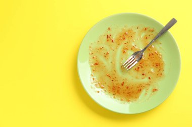 Sarı arka planda kirli bir tabak ve çatal, üst manzara.