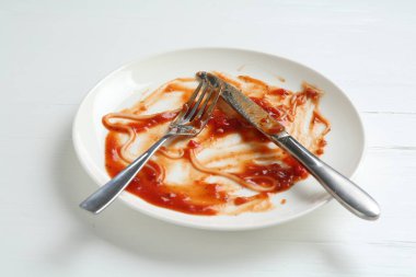 Kirli tabak ve çatal bıçak takımı beyaz ahşap masada, yakın plan.