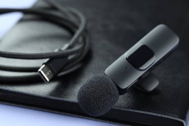 Açık mavi zemin üzerinde Lavalier mikrofon, kablo ve defter, yakın plan