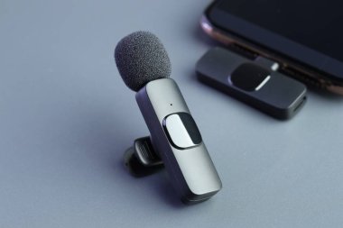 Açık gri arkaplanda Lavalier mikrofonlar ve akıllı telefon, yakın plan.