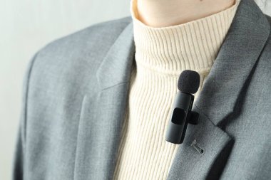 Gömleğinde lavalier mikrofon olan bir kadın açık gri arka planda, yakın plan.