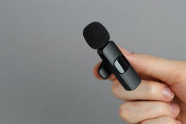Açık gri arka planda lavalier mikrofon tutan kadın, yakın plan. Metin için boşluk